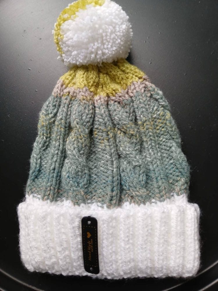 Cable-knit bobble hat in sage green with a chartreuse crown, a white cuff and a white and chartreuse bobble