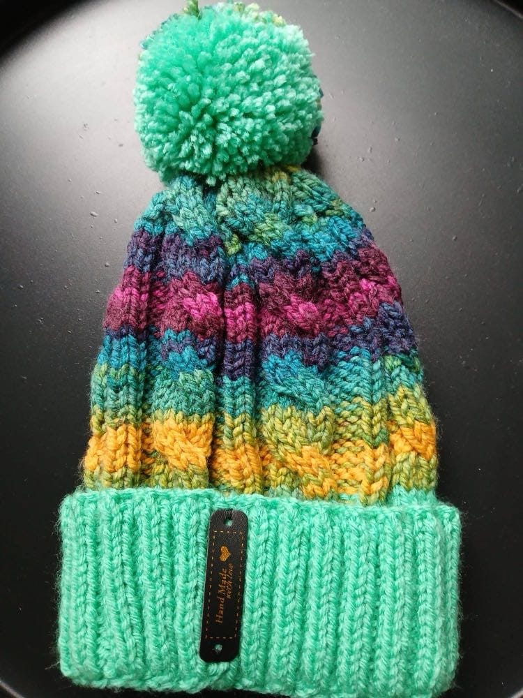 Cable-knit bobble hat striped teal, navy, magenta and mustard, with a seafoam cuff and seafoam bobble