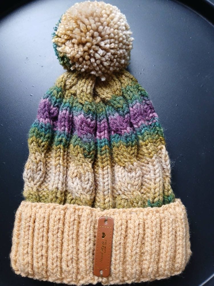 Cable-knit bobble hat striped oat, olive, teal and plum, with an apricot cuff and a sandy bobble
